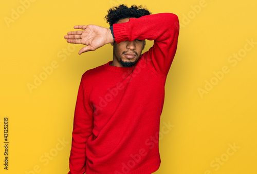 Young african american man with beard wearing casual winter sweater covering eyes with arm, looking serious and sad. sightless, hiding and rejection concept © Krakenimages.com