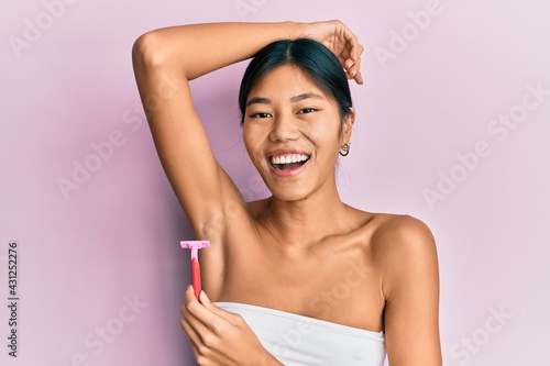 Young chinese woman wearing shower towel using razor smiling and laughing hard out loud because funny crazy joke. photo