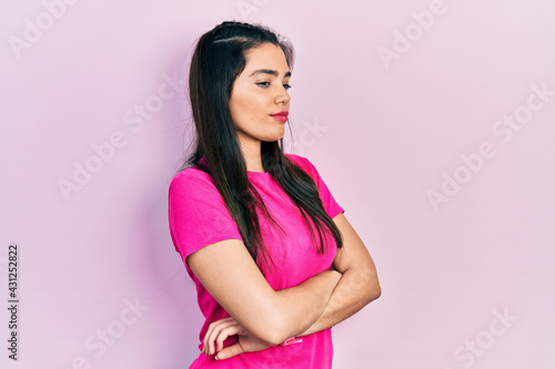 Young hispanic girl wearing casual pink t shirt looking to the side with arms crossed convinced and confident