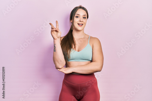 Young hispanic girl wearing sportswear smiling with happy face winking at the camera doing victory sign. number two.