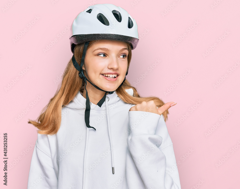 Beautiful young caucasian girl wearing bike helmet smiling with happy face looking and pointing to the side with thumb up. Beautiful young caucasian girl wearing bike helmet smiling with happy face looking and pointing to the side with thumb up.