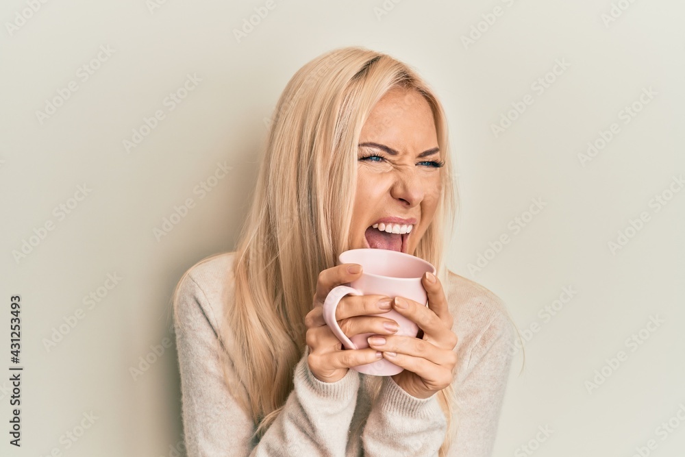 Young blonde woman drinking a cup of coffee angry and mad screaming frustrated and furious, shouting with anger. rage and aggressive concept. Young blonde woman drinking a cup of coffee angry and mad screaming frustrated and furious, shouting with anger. rage and aggressive concept.