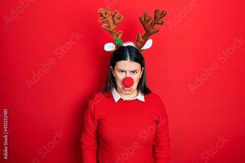 Young hispanic woman wearing deer christmas hat and red nose depressed and worry for distress, crying angry and afraid. sad expression.