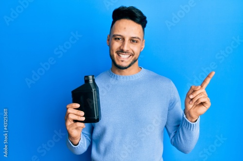 Young arab man holding motor oil bottle smiling happy pointing with hand and finger to the side