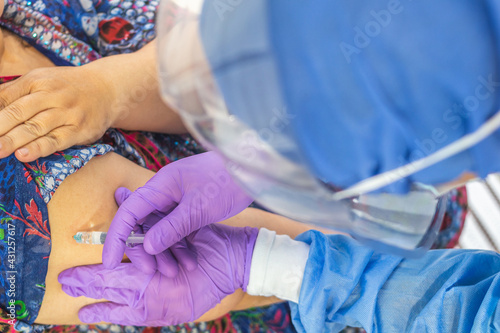 Top view of the hands of a doctor or nurse with surgical gloves  mask and face protection vaccinating a person in his arm with a syringe. Vaccination and coronavirus concept