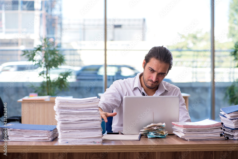 Young male employee unhappy with excessive work in the office Young male employee unhappy with excessive work in the office