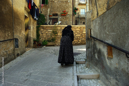 An elderly woman in a characteristic dress walks slowly through the streets of the village. Scanno, Abruzzo, Italy.