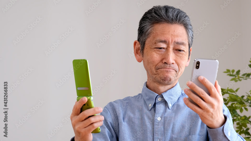 スマホとガラケーを比較するシニア男性 スマホとガラケーを比較するシニア男性