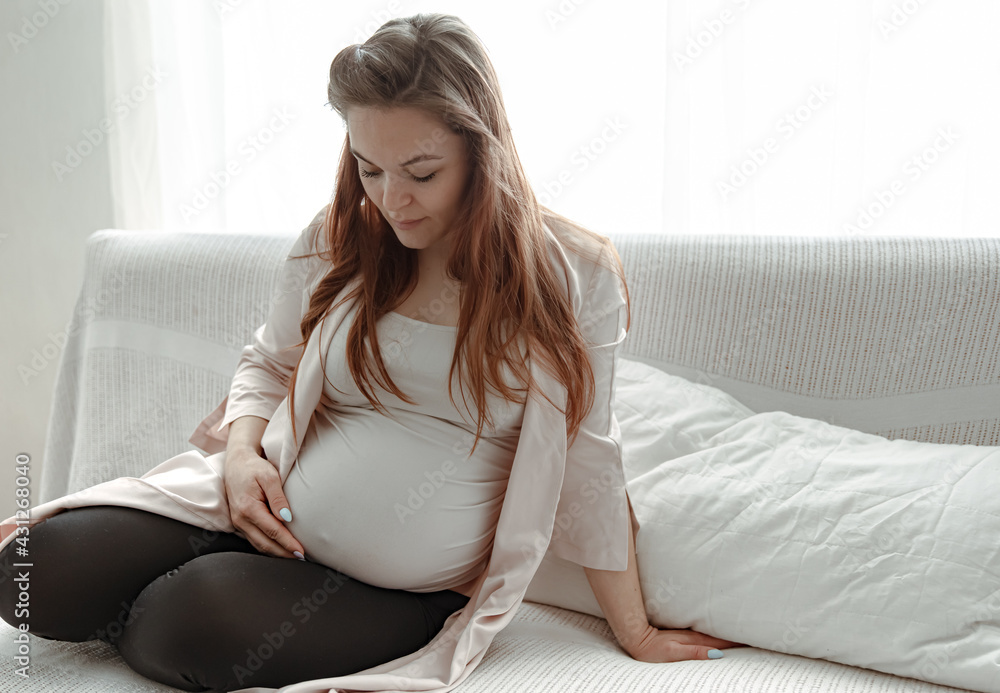 Stylish pregnant woman with a big belly sits on the couch at home. Stylish pregnant woman with a big belly sits on the couch at home.