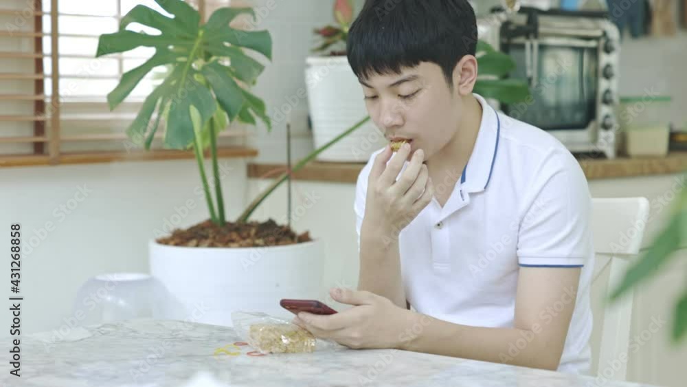Asian teen boy eating snacks While using the phone at the same time Asian teen boy eating snacks While using the phone at the same time