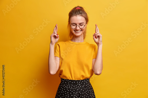 Фотография Cheerful amused millennial girl crosses fingers hopes dreams come true or wish f