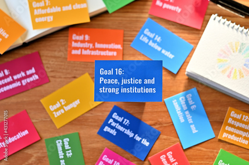 There is a card with the statement Goal 16:Peace, justice and strong institutions on table one of the goals of the SDGs and a symbol.