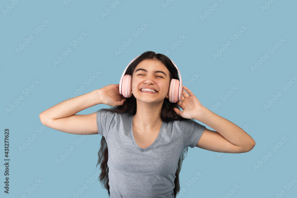 Happy Indian teenager in modern wireless headphones enjoying popular song in audio app, listening to music Happy Indian teenager in modern wireless headphones enjoying popular song in audio app, listening to music