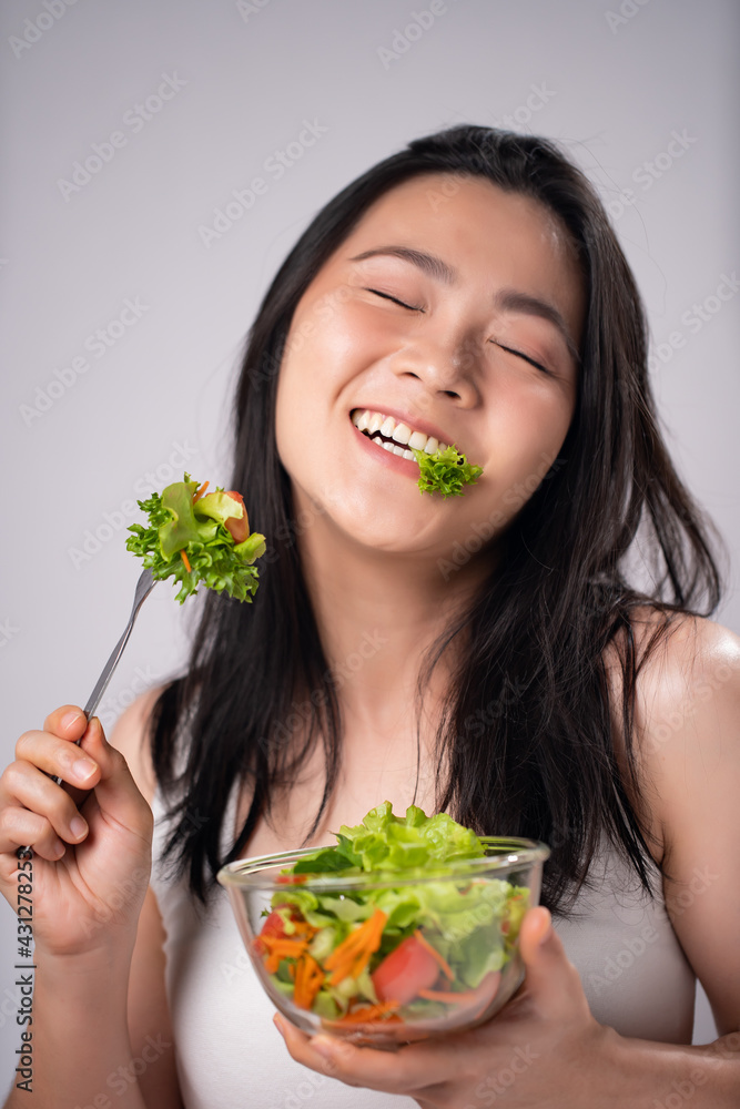 Asian woman eating salad isolated over white background. Asian woman eating salad isolated over white background.