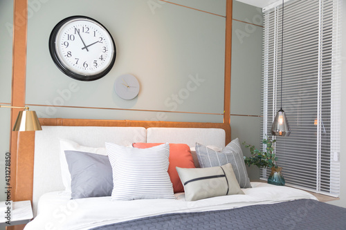 Stylish interior of modern bedroom. White, grey and pastel orange design pillow setting in cozy bedroom with clock on the wall.