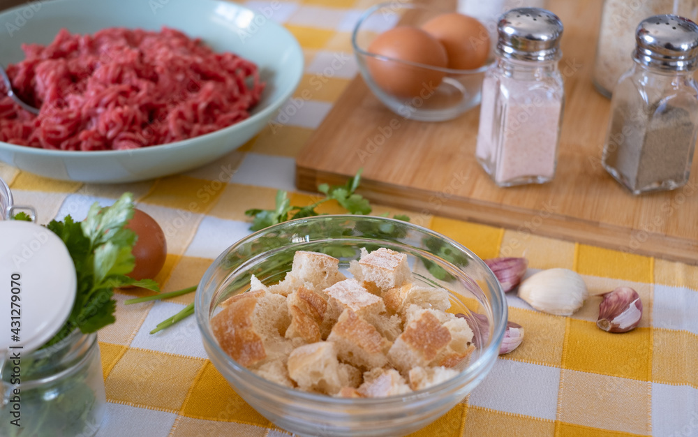 Close up on preparation of meatballs with raw materials to mix, home kitchen and yellow tablecloth Close up on preparation of meatballs with raw materials to mix, home kitchen and yellow tablecloth