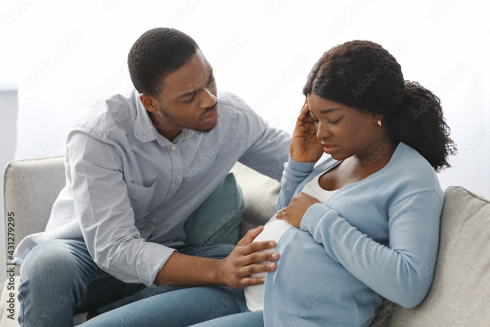 Black pregnant lady feeling sick, worried husband sitting by her Black pregnant lady feeling sick, worried husband sitting by her