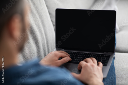 Man reclining on couch, using laptop with blank screen