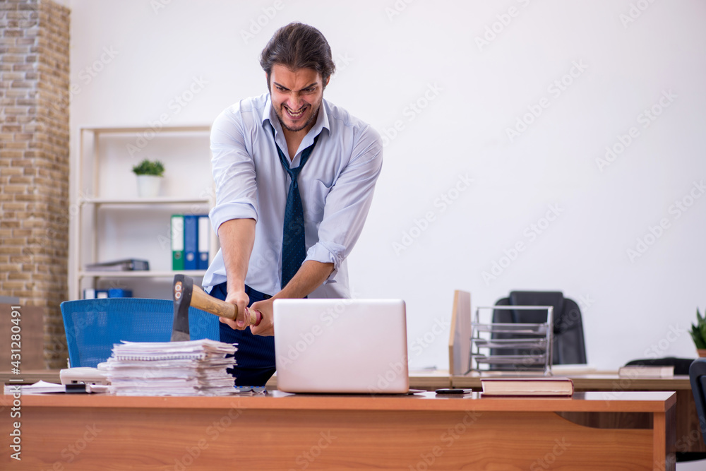 Young male furious employee holding hatchet in the office Young male furious employee holding hatchet in the office