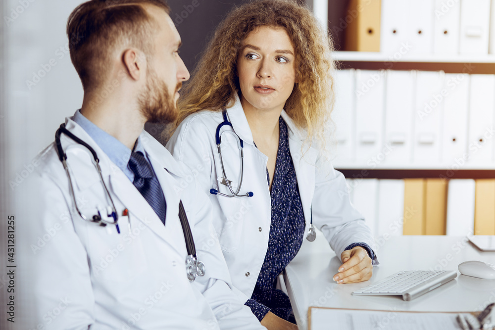 Bearded doctor with female colleague discussing current disease therapy while sitting at working place in sunny clinic. Team work in medicine Bearded doctor with female colleague discussing current disease therapy while sitting at working place in sunny clinic. Team work in medicine