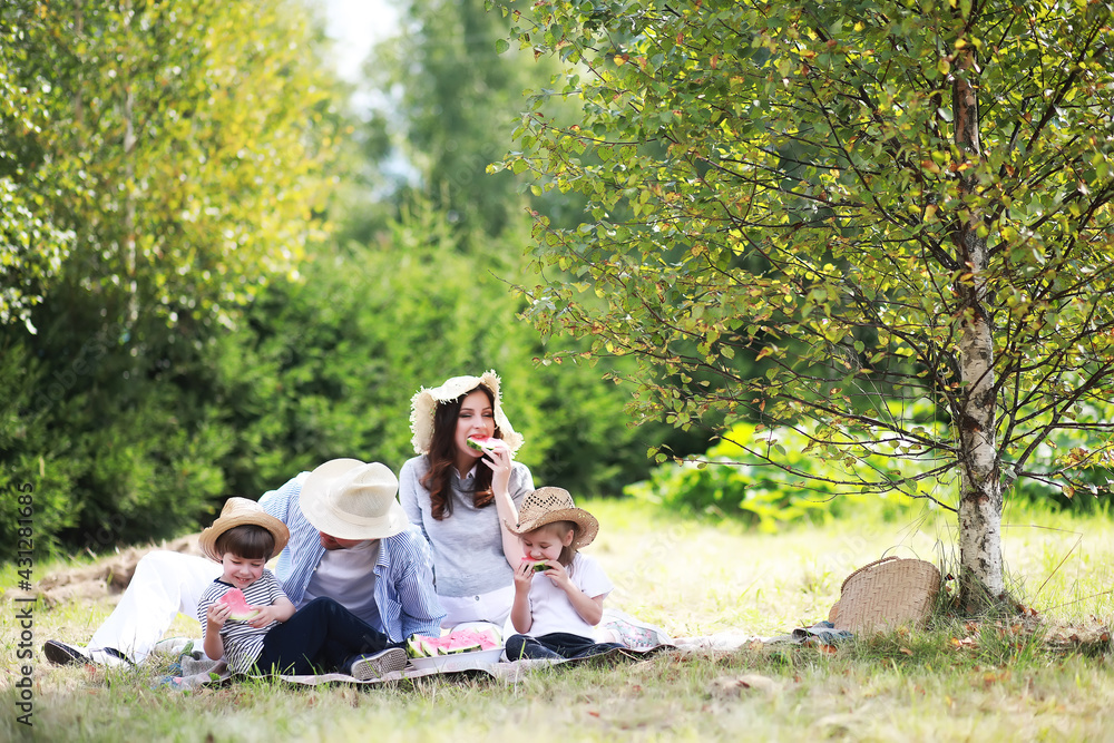 Happy family with children having picnic in park, parents with kids sitting on garden grass and eating watermelon outdoors Happy family with children having picnic in park, parents with kids sitting on garden grass and eating watermelon outdoors