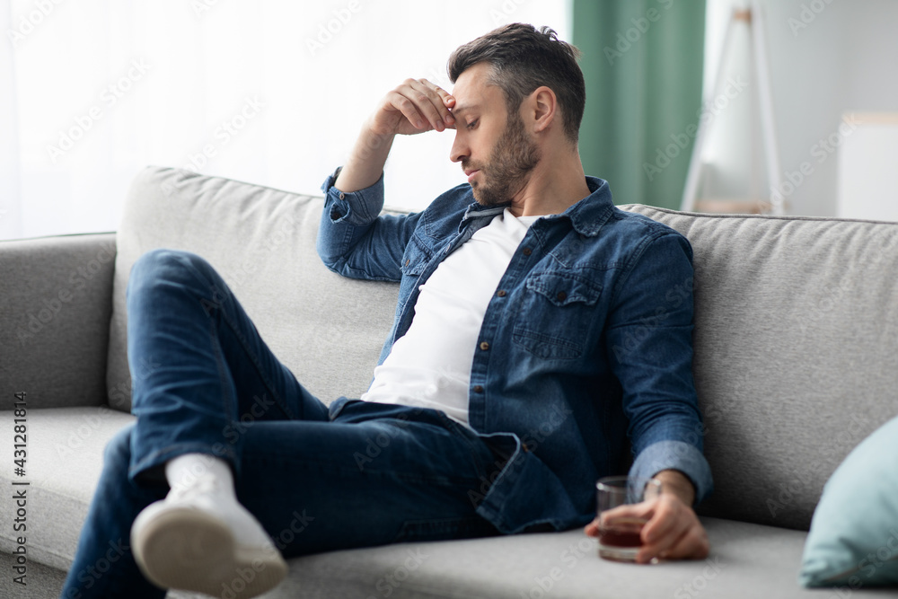 Depressed middle-aged man sitting on couch with glass of alcohol Depressed middle-aged man sitting on couch with glass of alcohol