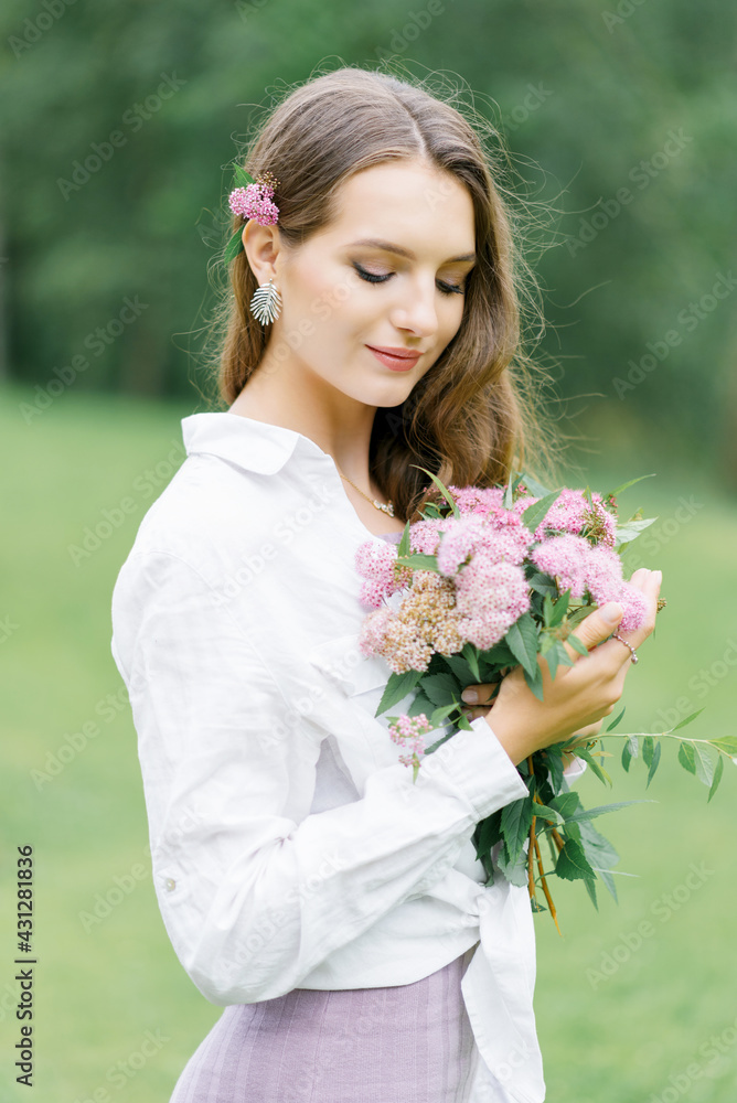Young girl stand at park background with bouquet of pink spireya flowers Young girl stand at park background with bouquet of pink spireya flowers