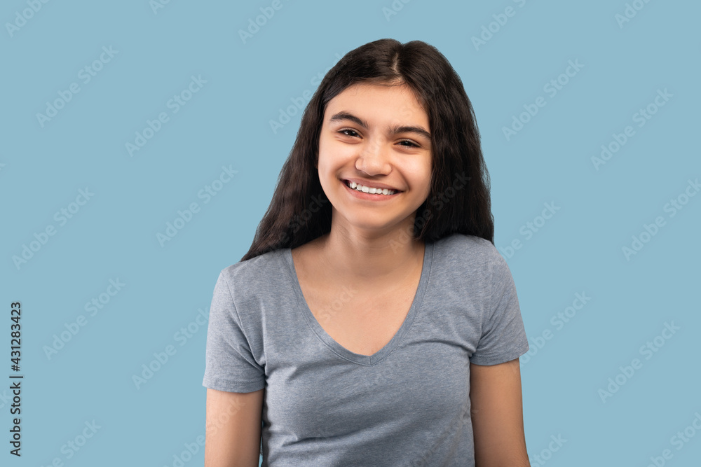 Beautiful Indian teenage girl with dark long hair smiling and looking at camera on blue studio background Beautiful Indian teenage girl with dark long hair smiling and looking at camera on blue studio background