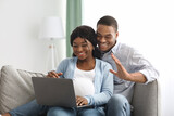 Cheerful pregnant black couple having video call, using laptop