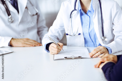 Unknown woman-doctor with male colleague are consulting patient woman while sitting at the desk in modern clinic, close-up. Perfect medical service, medicine during Coronavirus pandemic. Covid 2019