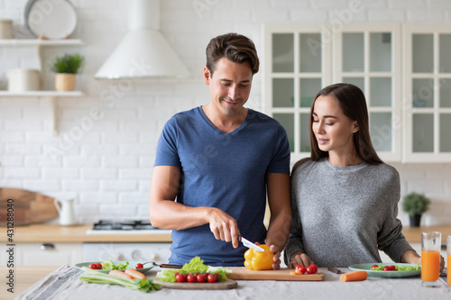 Beautiful young couple smiling while preparing vegetable salad in the kitchen at home.