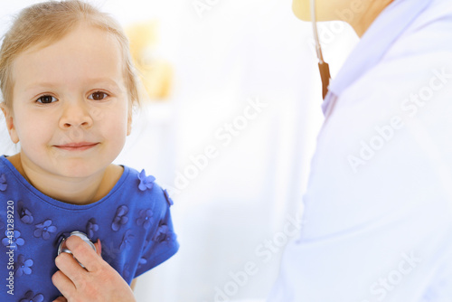 Doctor examining a little girl by stethoscope. Happy smiling child patient at usual medical inspection. Medicine and healthcare concepts