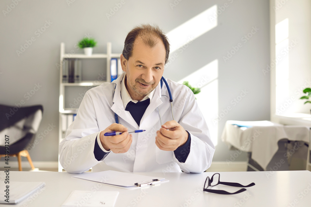 Male doctor in white coat with stethoscope sitting at desk explaining prescription consulting patient online headshot. Specialist giving expert advice looking at camera making video call from office