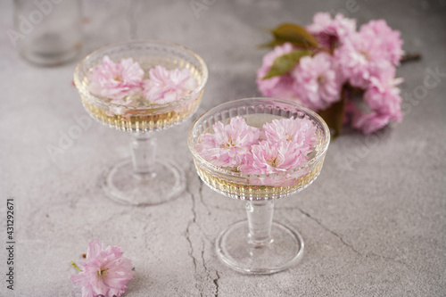 Two champagne glasses and pink cherry blossom on a grey surface