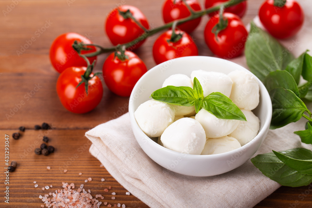 ingredients for caprese salad, mozzarella balls, cherry tomatoes on a branch, fresh basil, spices on a wooden background, horizontal ingredients for caprese salad, mozzarella balls, cherry tomatoes on a branch, fresh basil, spices on a wooden background, horizontal