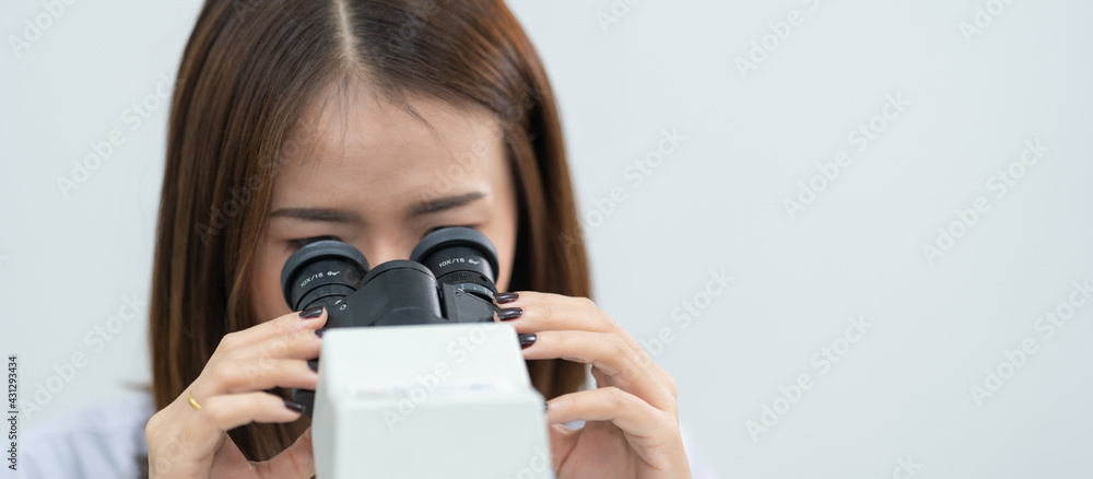 A young scientist woman in a laboratory coat looking through a microscope in a laboratory to do research and experiment. Scientist working in a laboratory. Education stock photo A young scientist woman in a laboratory coat looking through a microscope in a laboratory to do research and experiment. Scientist working in a laboratory. Education stock photo