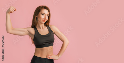 Fitness girl smiling in black sportswear on a pink background. Slim woman with a beautiful athletic body and tanned skin