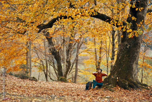 woman in autumn forest sitting under a tree landscape yellow leaves model