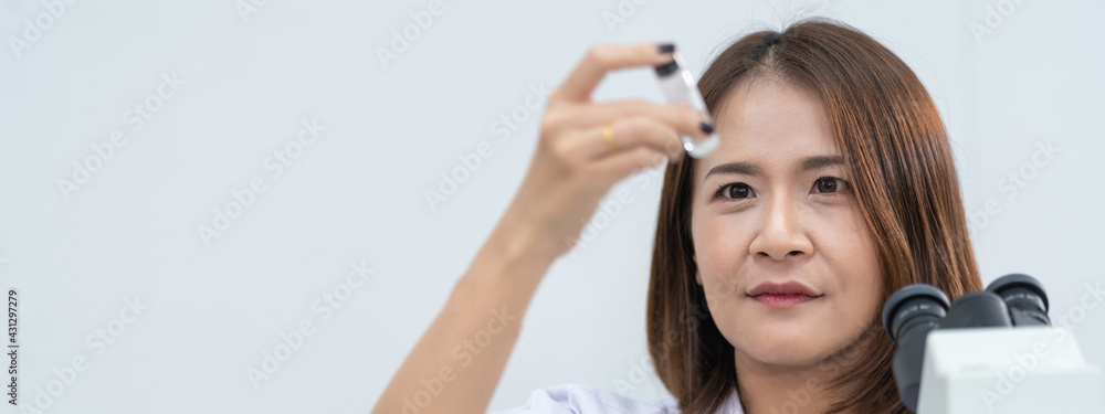 A young scientist woman in a laboratory coat looking through a microscope in a laboratory to do research and experiment. Scientist working in a laboratory. Education stock photo A young scientist woman in a laboratory coat looking through a microscope in a laboratory to do research and experiment. Scientist working in a laboratory. Education stock photo