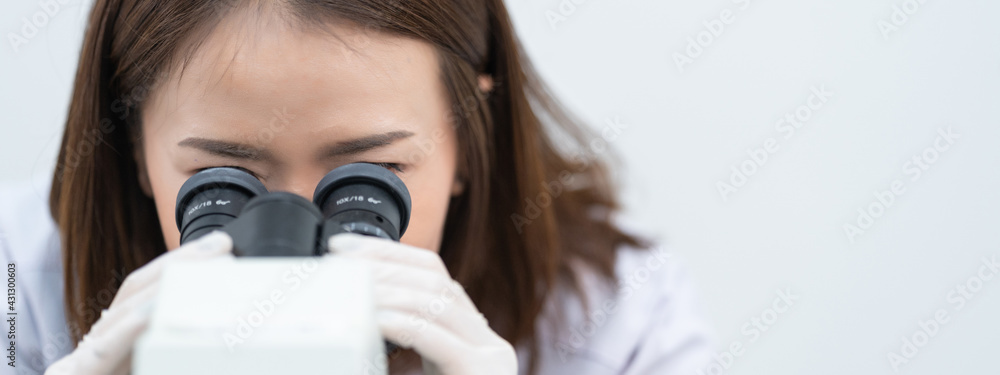 A young scientist woman in a laboratory coat looking through a microscope in a laboratory to do research and experiment. Scientist working in a laboratory. Education stock photo A young scientist woman in a laboratory coat looking through a microscope in a laboratory to do research and experiment. Scientist working in a laboratory. Education stock photo