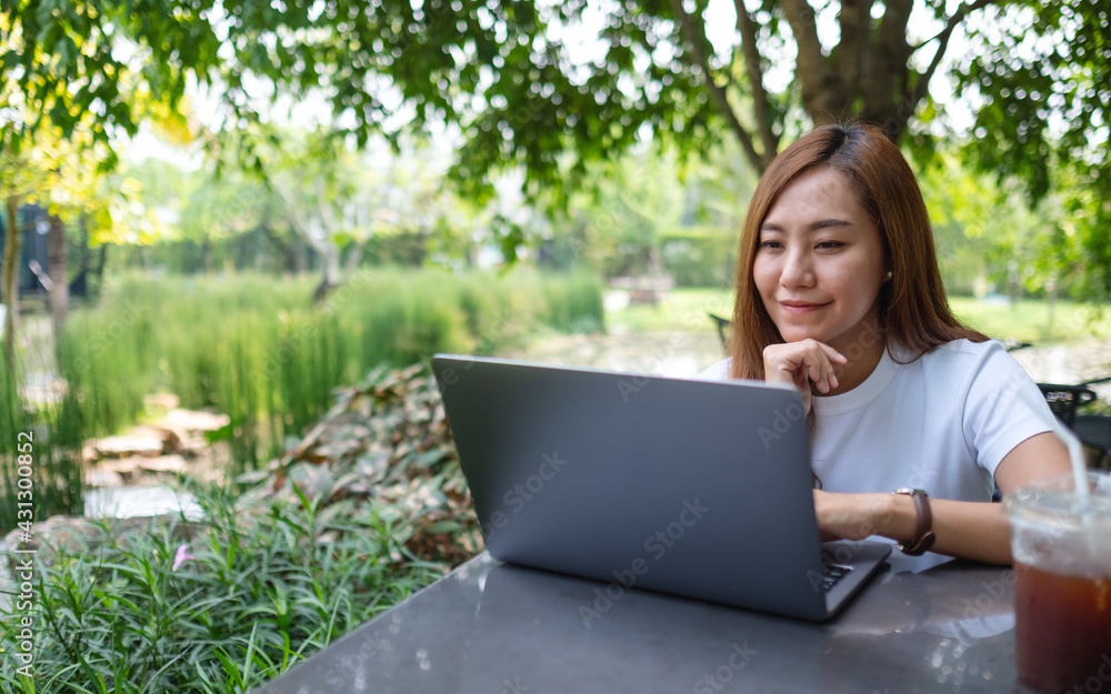 A young asian woman using and working on laptop while sitting in the park A young asian woman using and working on laptop while sitting in the park