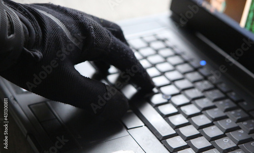 Computer hacker with black glove is typing on keyboard of notebook (focus on the glove).