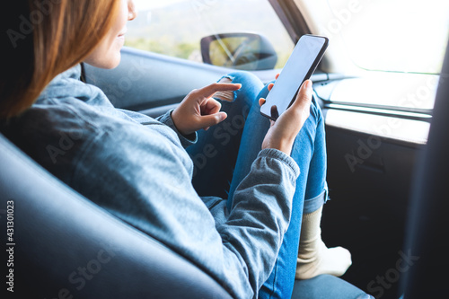 Closeup image of a woman holding and using mobile phone while riding the car