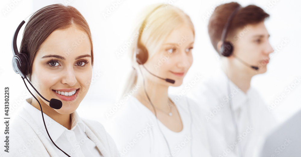Call center in sunny office. Group of diverse operators at work. Beautiful woman in headset communicating with customers of telemarketing service Call center in sunny office. Group of diverse operators at work. Beautiful woman in headset communicating with customers of telemarketing service