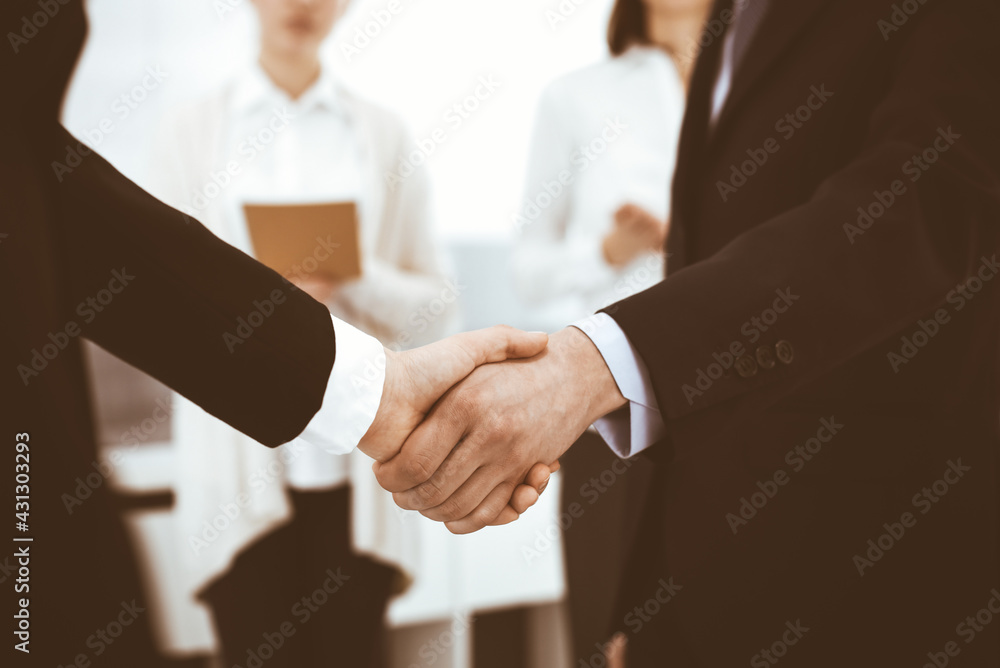 Businessman and woman shaking hands with colleagues at the background. Handshake at meeting in office. Concept of success in business