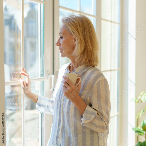 Wallpaper Mural Enjoying new day. Side view of thoughtful beautiful mature woman holding cup of coffee or tea, looking in window and thinking or dreaming about something while spending free time in morning at home Torontodigital.ca