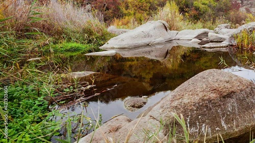 Autumn trees and large stone boulders around. A water cascade in autumn creek with fallen leaves. Water flows around the stones in the river. Aktovsky Canyon, Ukraine. photo