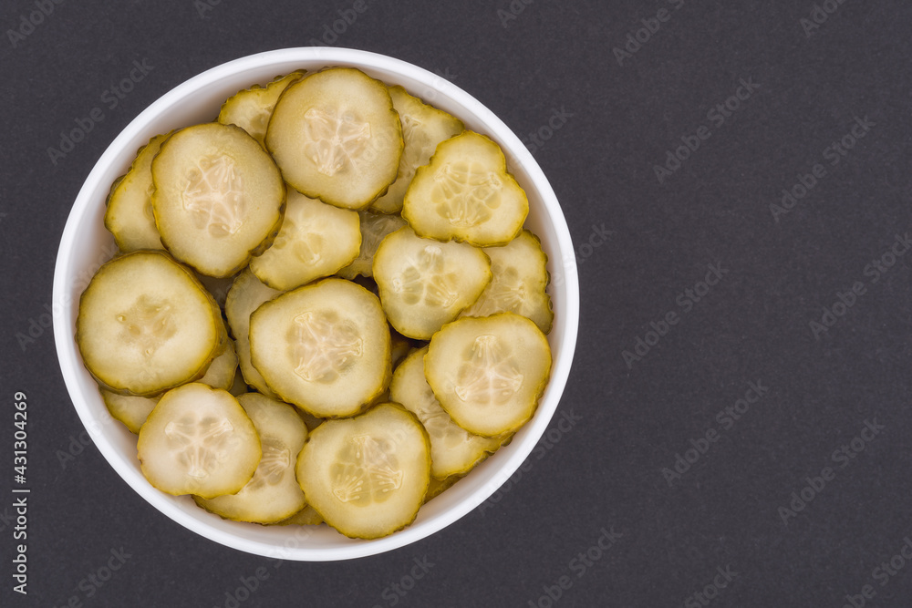 White glass bowl of sliced salted cucumber. Isolated on a dark grey background. Top view close up White glass bowl of sliced salted cucumber. Isolated on a dark grey background. Top view close up