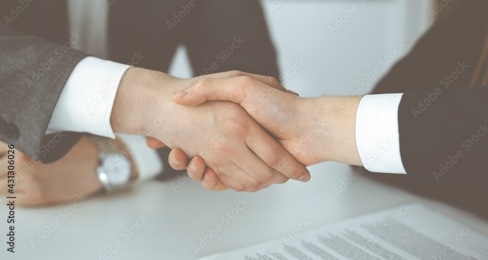 Unknown businessman shaking hands with his colleague or partner above the glass desk in modern office, close-up. Business people group at meeting Unknown businessman shaking hands with his colleague or partner above the glass desk in modern office, close-up. Business people group at meeting