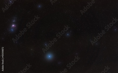 Winter night sky with purple Orion nebula, bright blue Rigel star - diffused through some clouds - in bottom lower part, long exposure photo photo